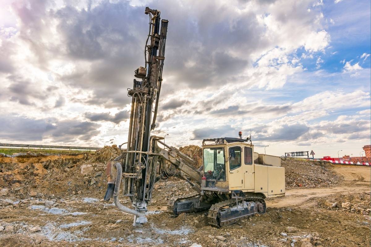 A geotechnical engineering in a hardhat and high-visibility vest examines a soil core sample next to a drilling rig on an infrastructure construction site in Pakistan.